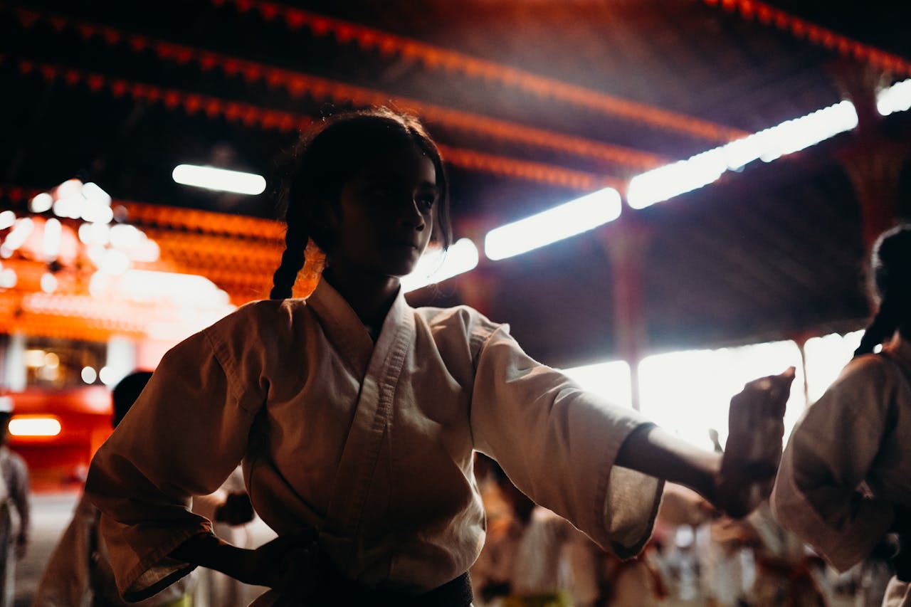 Focused young girl in martial arts uniform practices in an indoor dojo setting.